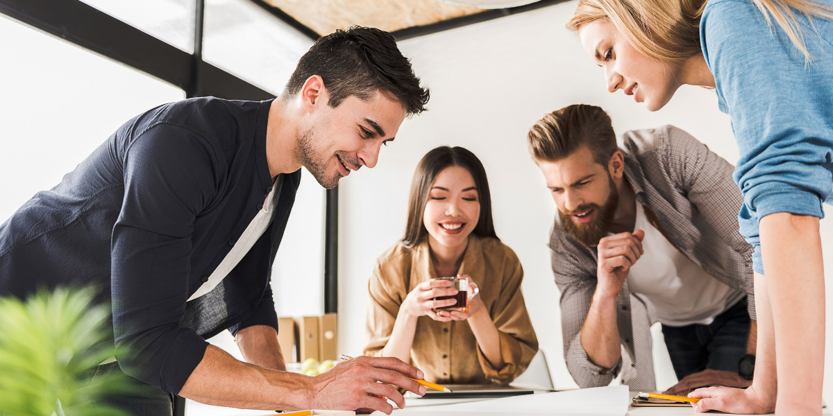 Four casually dressed individuals gathered around a table discussing a document.
