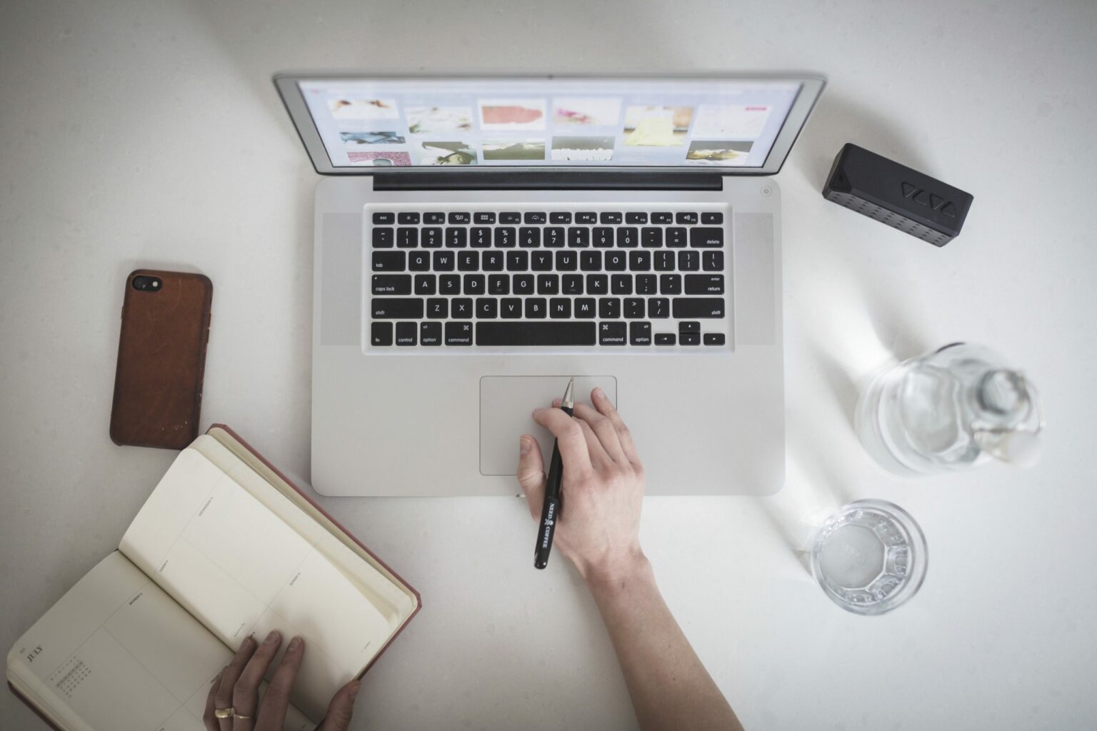 Overhead photo of a user working on a laptop with a notebook, pen, and glass of water nearby