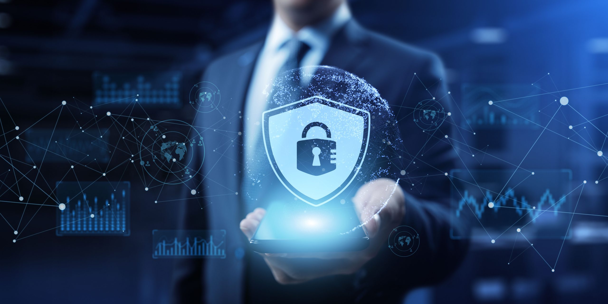 A business-suited individual holds a glowing digital tablet in their hands. Hovering above the tablet is a translucent shield icon with a padlock at its center. Surrounding the shield are abstract network graphics—connecting nodes, data charts, and world map symbols—suggesting secure digital connections and global cybersecurity.